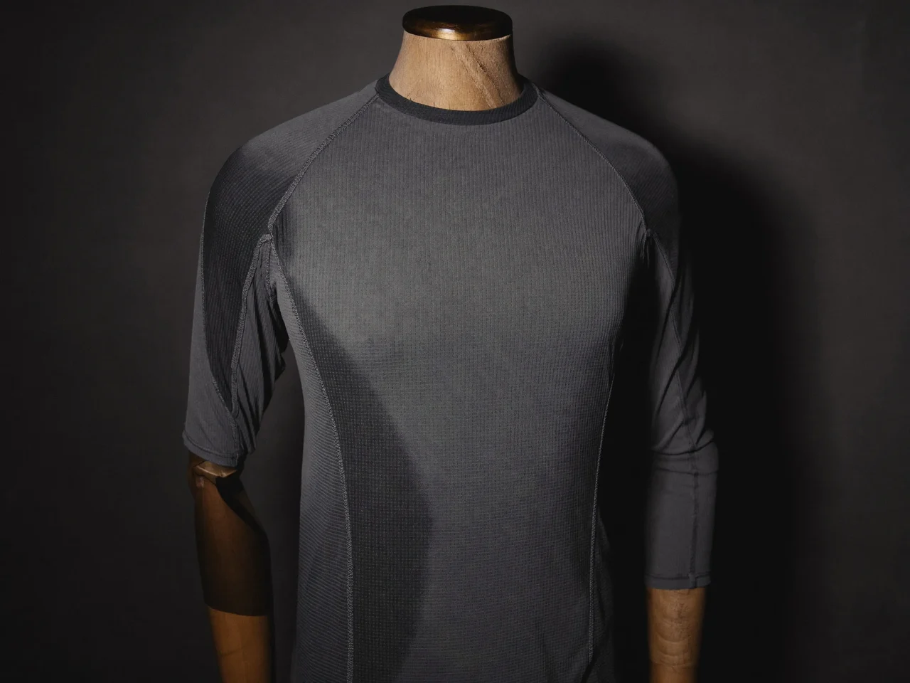 Maglia tecnica carbone su busto in legno contro una parete scura, illustrazione