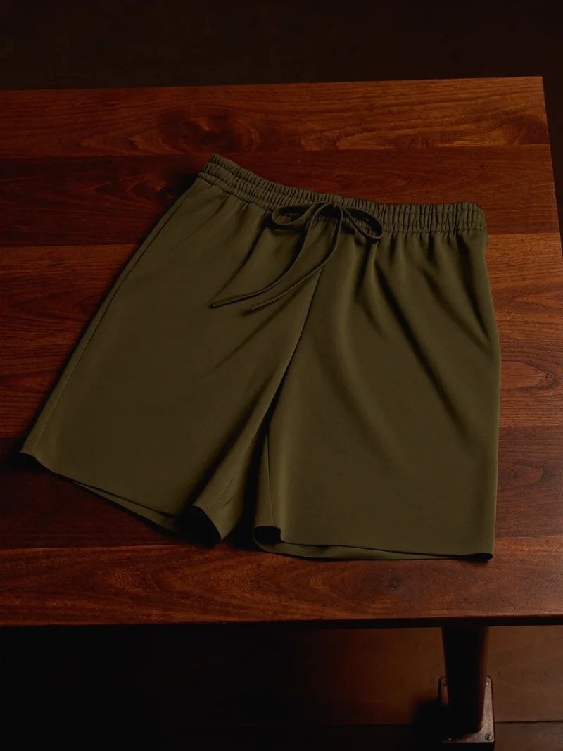 Pantaloncini verde oliva scuro stesi su un tavolo di noce con cordino